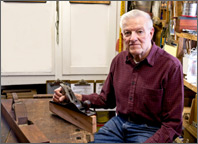 Photo of a man sitting at a workbench and holding tools. Copyright iStockphoto.com/Gene Krebs.
