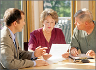 Photo of a couple sitting at a table and looking through paperwork while speaking with a consultant. Copyright iStockphoto.com/Edward Bock.