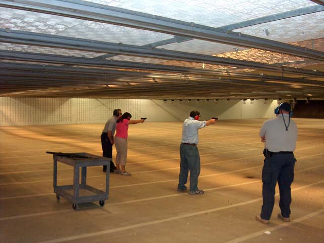 A photograph of two people firing a gun while two others advise and watch at the Federal Law Enforcement Training Center.  