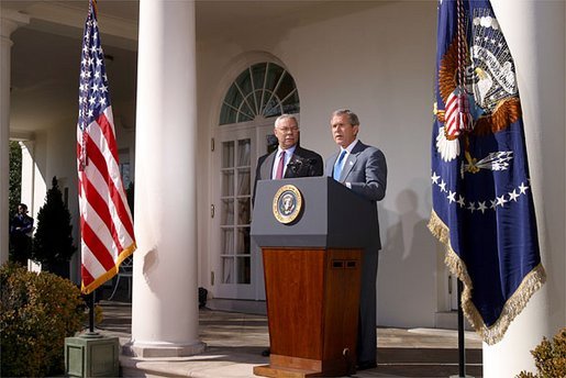 As Secretary of State Colin Powell stands by his side, President George W. Bush addresses the media in the Rose Garden Friday, March 14, 2003. White House photo by Paul Morse