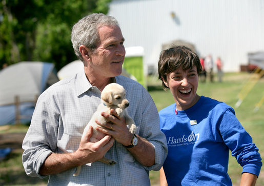 President George W. Bush holds the offspring of a stray dog during a tour of the animal rescue area of the Hands On Network base camp in Biloxi, Mississippi, Thursday, April 27, 2006. Pictured with the President is Disaster Response Coordinator Erika Putinsky. White House photo by Eric Draper