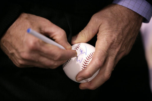 After warming up with a few pitches, President George W. Bush signs a baseball shortly before throwing one over the plate for the opening game between the Cincinnati Reds and the Chicago Cubs in Cincinnati, Ohio, Monday, April 3, 2006. White House photo by Eric Draper