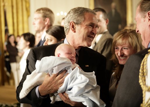 President George W. Bush holds one-month-old Trey Jones as he greets the audience Tuesday, May 24, 2005, after remarks on bioethics in the East Room of the White House. White House photo by Eric Draper