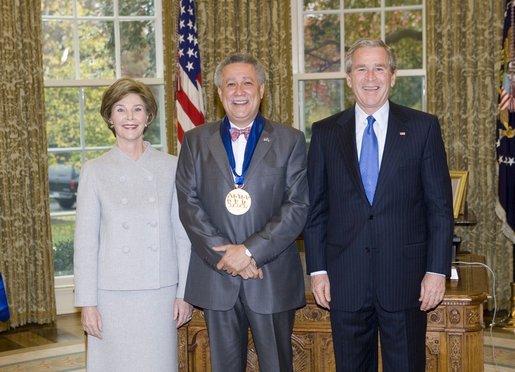 President George W. Bush and Laura Bush stand with jazz musician Paquito D'Rivera, recipient of the 2005 National Medal of Arts, in the Oval Office Thursday, Nov. 10, 2005. White House photo by Eric Draper