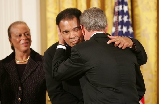As Mrs. Lonnie Ali looks on, President George W. Bush embraces three-time heavyweight boxing champion of the world Muhammad Ali after presenting him with the Presidential Medal of Freedom Wednesday, Nov. 9, 2005, during ceremonies at the White House. White House photo by Paul Morse