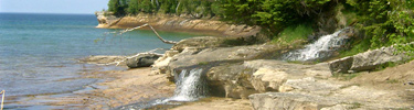 A waterfall trickles over the escarpment as the Pictured Rocks cliffs rise again after Miners Beach.