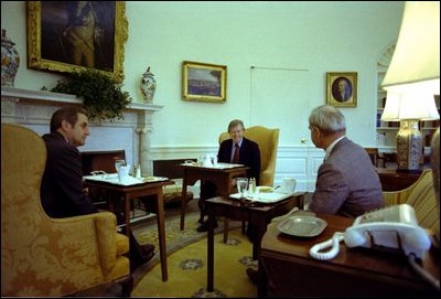 While sitting in front of the fireplace in the Oval Office February 7, 1977, President Jimmy Carter hosts a lunch for Vice President Mondale and energy adviser James Schlesinger. Hanging above the mantel is Charles Willson Peale's portrait of George Washington, which President Carter acquired for the White House's permanent art collection.