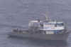 A fishing vessel with a grey hull and white superstructure with migrants onboard.
