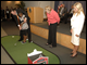 Phil Mickelson teaches a young student about putting while Secretary Margaret Spellings and Amy Mickelson encourage her.