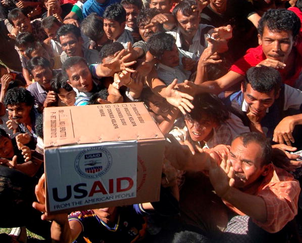 A photograph of many tsunami victims reaching for a box labeled USAID.  