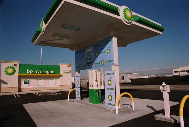 A picture of a hydrogen refueling station consisting of a single pump and  dispensing unit centered on a narrow, slightly elevated concrete island flanked by protective  steel bollards.  Vertical beams in the island support a weather-protective  overhang extending over vehicle refueling pads on each side of the dispensing  unit.  The design resembles a typical gasoline refueling station.