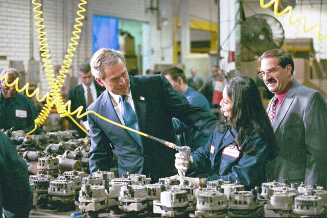 A photograph of President Bush talking with an employee at U.S.A. Industries in Bay Shore, N.Y., while she is working on components.  