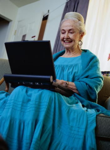 Photo of a senior citizen sitting on her couch at home and using a laptop computer.
