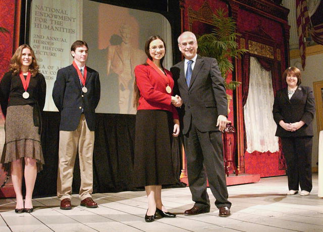 A photo of NEH Chairman Bruce Cole on stage shaking hands and congratulating winners of the 2004 The Idea of America essay contest for high school students.