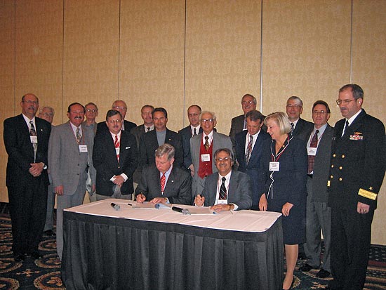 Seated (L to R): Malcolm P. Branch, President, Virginia Ship Repair Association and Leo Edwards, Acting Area Director, OSHA Norfolk Area Office. Standing to the right of the signing table: U. S. Congresswoman, Thelma Drake and Rear Admiral John Clarke Orzalli, Commander, Mid-Atlantic Regional Maintenance Center. Standing behind the signatories are several of the partnership participants.