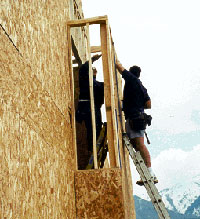 Construction worker on a portable ladder at proper angle against building under construction