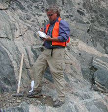 USGS Geologist Wayne Premo collecting samples of Lower Proterozoic felsic gneiss (gray, layered rock) and amphibolite (black rock) in Clear Creek Canyon west of Denver.