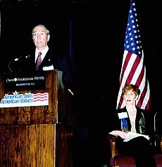 John Nau speaks at a podium while session moderator Lora Lee Martin looks on.