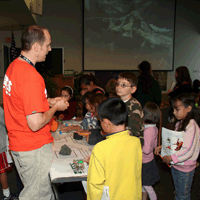 Scientist explaining rocks to kids, movie of Hawaiian lava playing in background in non-ideal lighting.