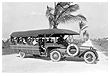 Picture taken in the 1930s of a bus on a beach, with a palm tree in the background.