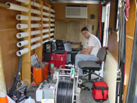 USGS scientist processing preliminary borehole radar data inside a trailer used to house borehole radar equipment. White pipes on the left are for antenna storage