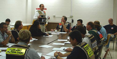 People around a meeting table wearing identifying vests.