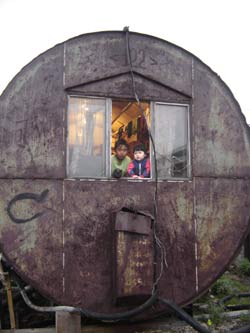 Photo of children leaning out the window of their hazardous waste drum converted into living space