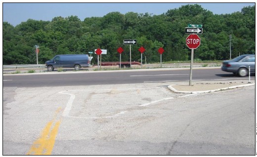 Photograph of a T-intersection treated with a channelized right turn lane, one-way signs, and a closed median with reflective markers and a raised curb.