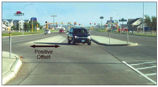 Photograph of a road design where the left turn lanes are offset from the through lanes, allowing left turning vehicles going in each direction to see oncoming traffic.