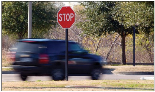 Blurred photograph of a vehicle moving past a STOP sign without stopping.