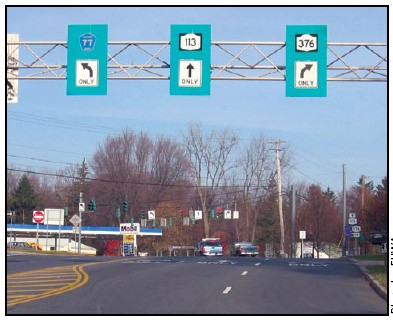 Photo of lane assignment signs on a mast arm above the roadway in advance of a signal. Signs indicate which lane vehicles should be in to reach specified routes.