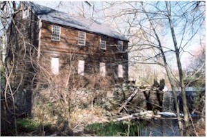 Photograph of an old log cabin adjacent to a stream.