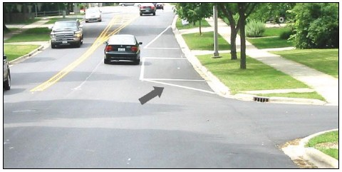 Photo depicts a painted box on the roadway at the corner of a neighborhood intersection that prohibits vehicles from parallel parking within it so that sight distance will not be blocked for for left turning vehicles.