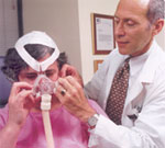 Dr. Jeffrey Hausfeld, M.D., adjusts a Continuous Positive Airway Pressure (CPAP) device for his patient.  The CPAP device treats obstructive sleep apnea by delivering continuous air pressure through the nasal passages to keep the upper airway open.