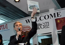 Secretary Gutierrez greeting tourists holding Department of Commerc commemorative book with "Welcome" banner in background. Click for larger image.
