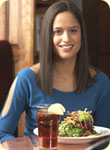 A woman at a table with salad and ice tea.