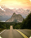 A roadway with a sunset behind the mountains on the horizon.