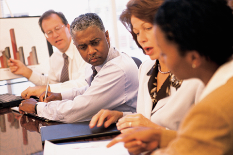 Photograph of four people, two men and two women, sitting side by side at a table in a meeting.