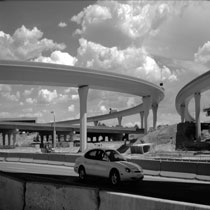 Picture depicts several overpasses on the "Big I" construction project. A vehicle is visible in the foreground, and a component of the ITS system is visible on the highest overpass.