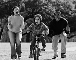 Picture of child learning to ride a bike with his parents encouraging him