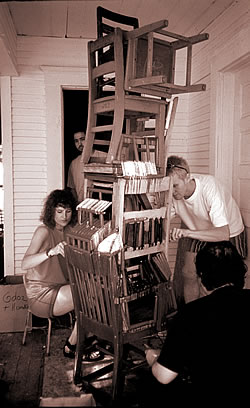 Three people work on a stack of chairs that towrs above their heads