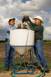 Technician (left) and welder prepare compost tea by pouring compost into an extractor: Click here for full photo caption.