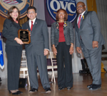 Photo of Lesvia Zambrana receiving an award from Attorney General Alberto R. Gonzales, Assistant Attorney General Regina B. Schofield, and OVC Director John W. Gillis.