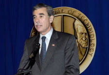Gutierrez speaking at microphone, with image of medal of technology in the background.