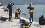 Some of the divers from the Regional Center for Underwater Demining (RCUD) during a training dive from a quay at the center. The RCUD in Bijela, Montenegro, a center for excellence, is the only such non-military humanitarian underwater node in the world. Its divers, and those that it trains, are able to safely recover and arrange for the proper destruction of munitions that have been dumped at sea, unexploded ordnance that remains hazardous even when underwater, sea mines, and landmines that in some cases may have washed up on beaches or been displaced into rivers, streams, and lakes by heavy rains. Some of the unexploded ordnance and munitions encountered by RCUD divers date back to World War II. [Regional Center for Underwater Demining]