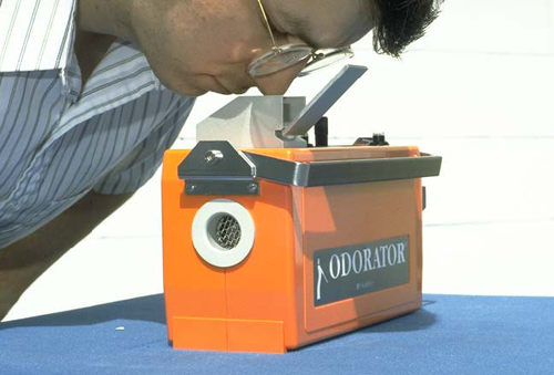 This man is conducting a sniff test using an odor testing instrument.