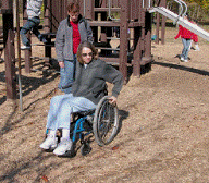 Photo of a person using a wheelchair testing out treated engineered wood fiber at a playground.