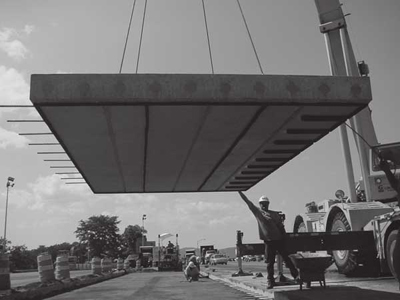 Photograph of road crew lowering precast panel into place on a highway.