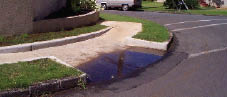 Case Study: Photo of dirty water that has backed up the slope of a curb ramp and stands in a pool at the toe, obscuring the joint at the gutter.