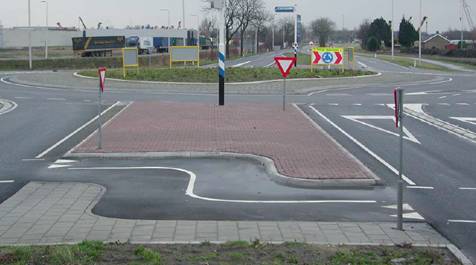 Figure 8.  Photo.  Jog in bicycle path in splitter island at turbo roundabout.   This photograph depicts a splitter island median where the crosswalk has an ‘s’ shape.  The crosswalk is striped and has raised curbs for positive guidance.  This design allows cyclists to complete their crossing closer to the circulatory roadway at the exit of the roundabout.  The purpose of the chicane is to slow cyclists while making their crossing.